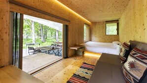 Interior de una cabaña moderna de madera, con cama, sofá y zona de comedor.