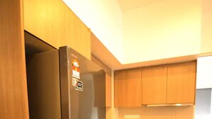 Une cuisine de taille réduite avec un réfrigérateur noir, des placards en bois et un lave-linge.