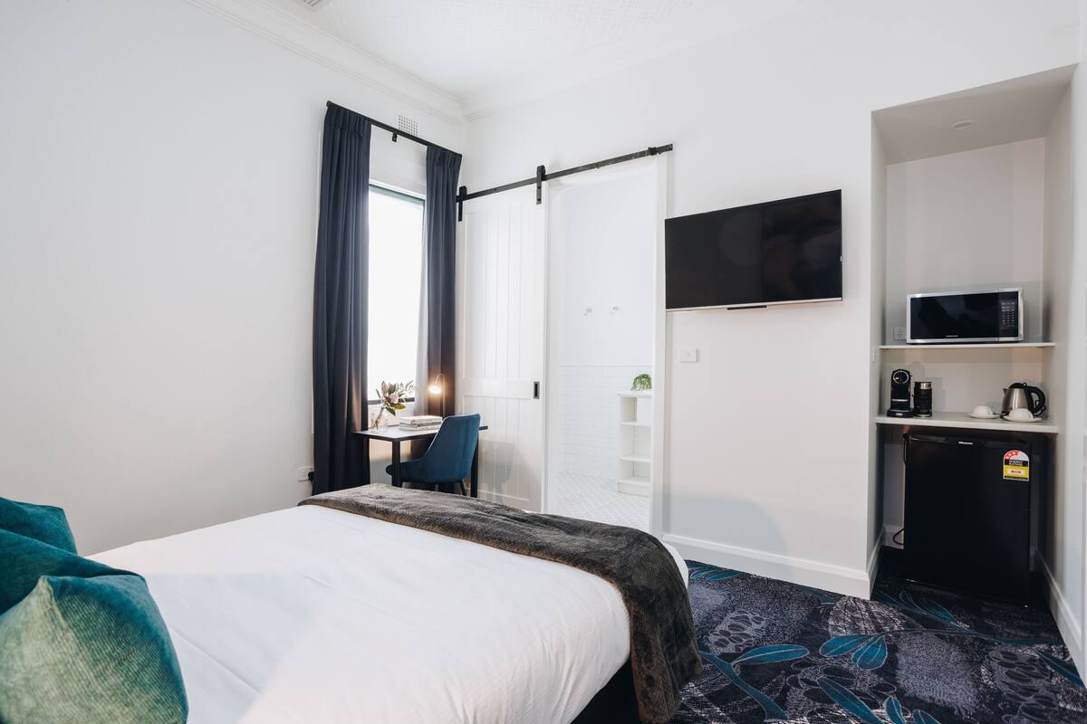 A hotel room with a bed, a desk with a chair, a TV, a microwave, and a refrigerator.