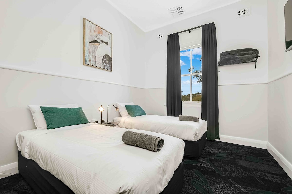 A hotel room with two beds, a large mirror, a window with curtains, and a view of the outdoors.