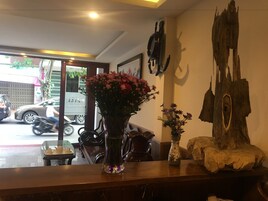 Uma área de recepção com um vaso de flores, uma escultura de madeira e um relógio na parede.