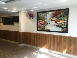 Um corredor com parede de painel de madeira, uma grande pintura emoldurada de uma paisagem colorida e um ventilador de pé.
