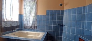 A bathroom with a bathtub, a shower, and a window with patterned curtains. - Jungla de Panama (Palmira)