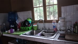 Una cocina con un lavamanos, una ventana y diversos utensilios.