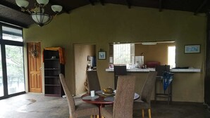 Comedor con una mesa redonda y cuatro sillas, cocina al fondo y una puerta que da al exterior.
