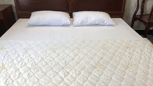 A neatly made bed with a quilted white bedspread featuring floral embroidery, two white pillows, and a wooden headboard. - Thinh Phuong Nam Hotel (Can Tho)