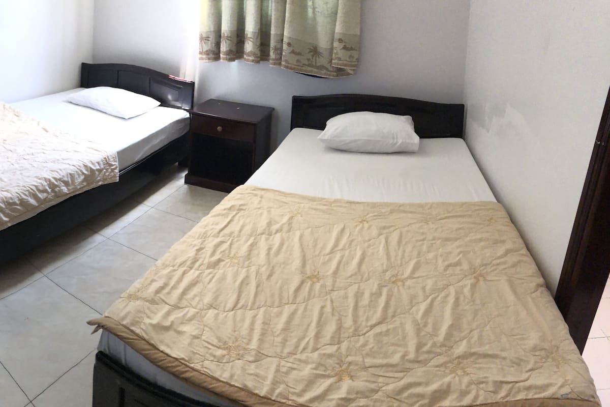Dos camas individuales con estructuras de madera en una habitación con suelo de baldosas.