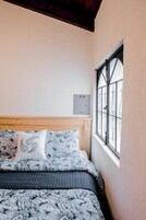 Un dormitorio con cama, ropa de cama estampada, una ventana con barrotes y un termostato en la pared.