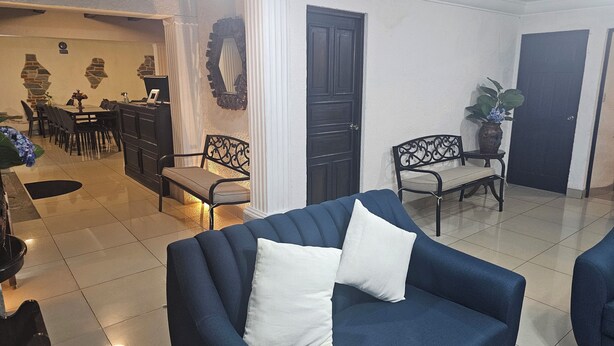 Ein Wohnzimmer mit einem blauen Sofa, einem Essbereich mit Stühlen und einem Tisch sowie einer dunkelholzigen Tür.