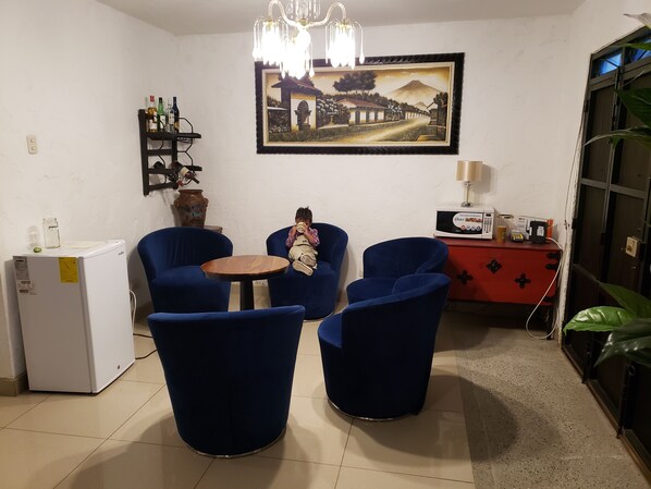 A room with a dining table, two blue chairs, a white refrigerator, a red cabinet, and a wall-mounted TV.