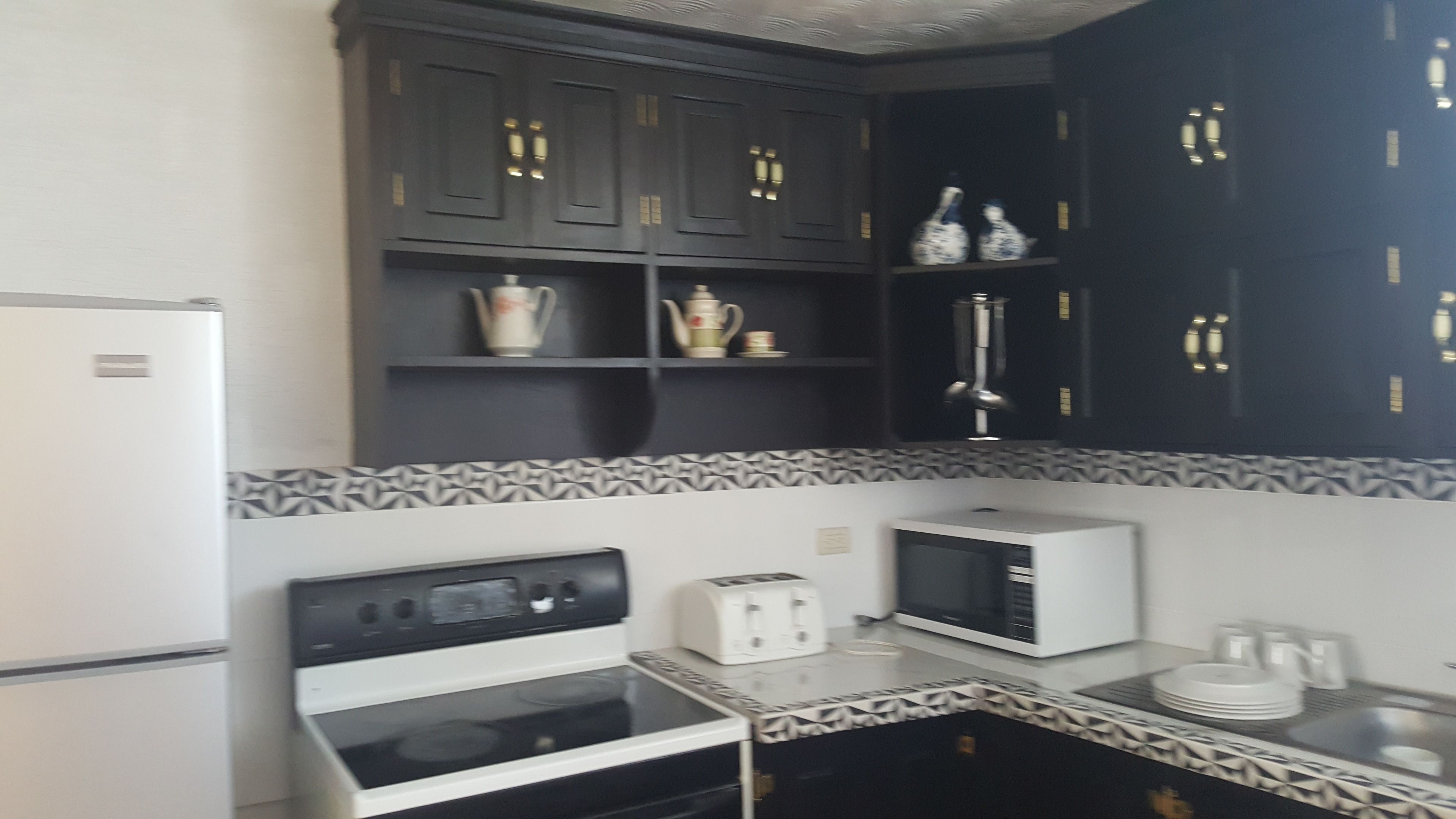 Una cocina equipada con refrigerador, estufa, microondas y tostadora. Hay armarios sobre la encimera con adornos.