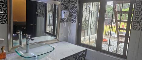 A bathroom with a glass sink, a large mirror, and a window with decorative iron bars.