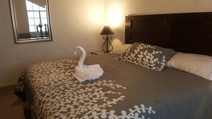 Une chambre d’hôtel avec un lit agrémenté d’une serviette en forme de cygne, une couvre-lit à motifs et une table de chevet avec une lampe.