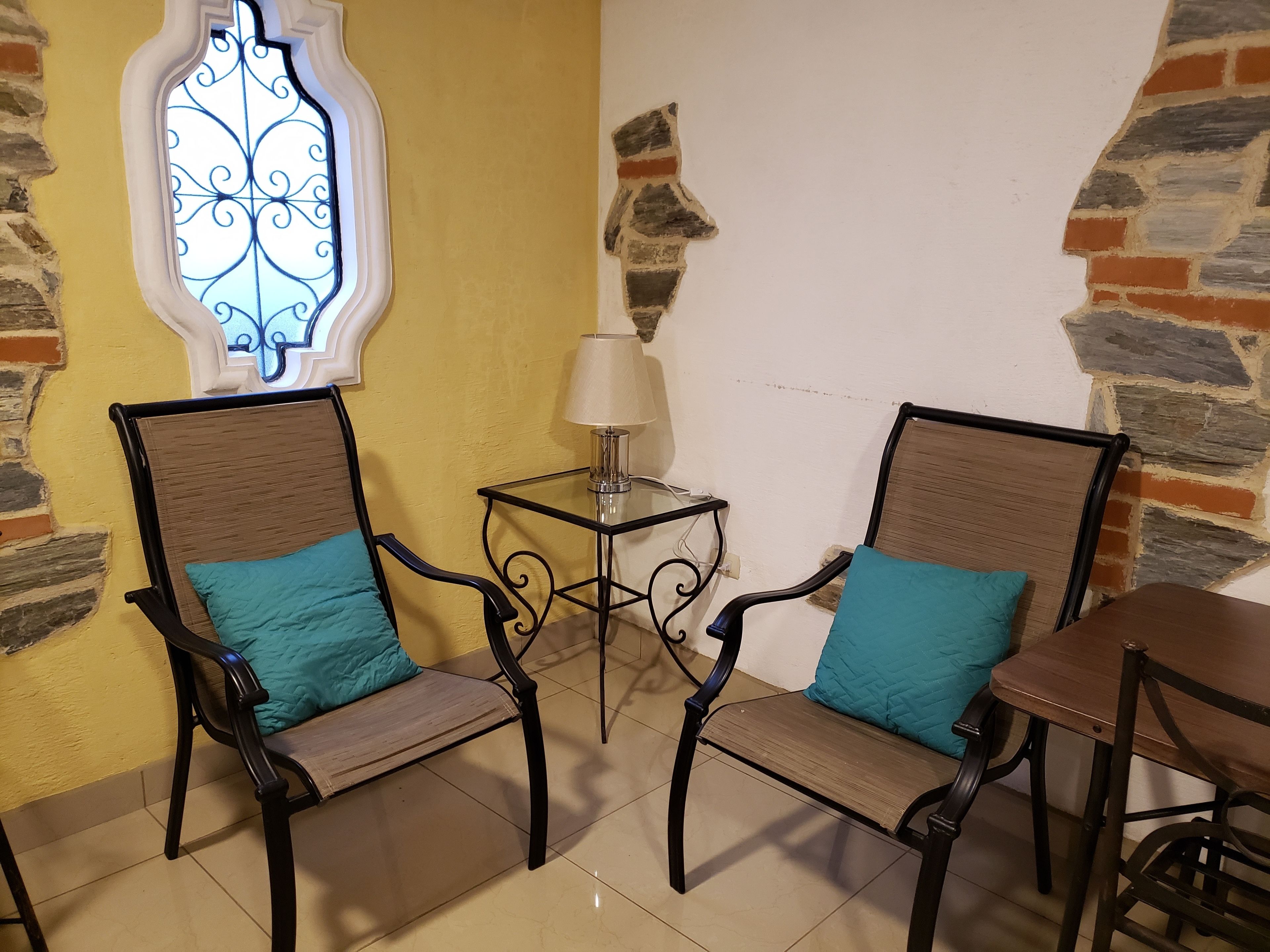 Due poltrone con cuscini color acquamarina, un tavolino con una lampada e una finestra con decorazioni in ferro battuto.