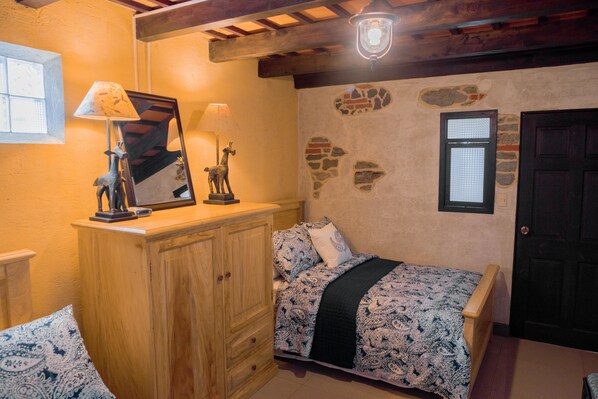 Une chambre à coucher avec un lit, une commode en bois et un mur en pierre.