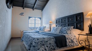 Ein Schlafzimmer mit einem großen Bett, einem Nachttisch, einer Lampe und einem Fenster mit Gitterstäben.