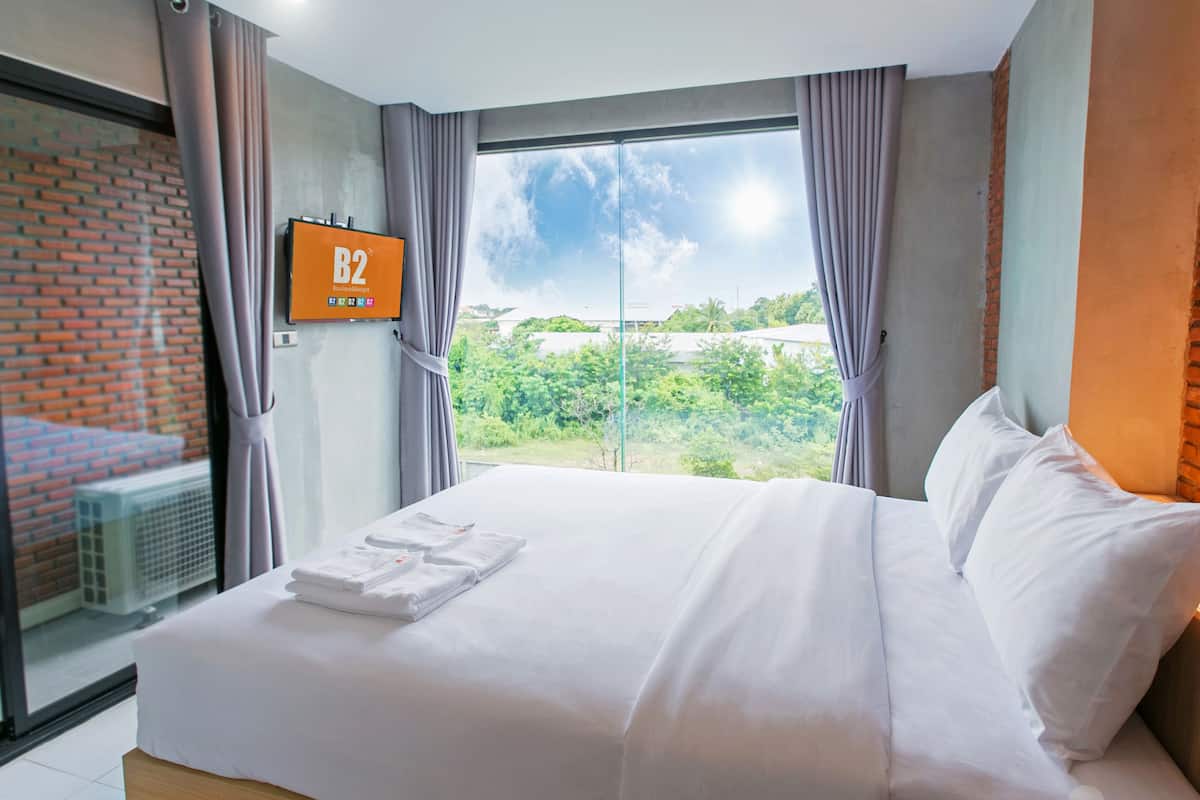 A hotel room with a bed, a TV, and a window with a view of greenery.