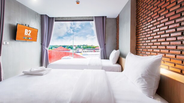 Habitación de hotel con una cama grande, un televisor en la pared y vistas a edificios a través del ventanal.
