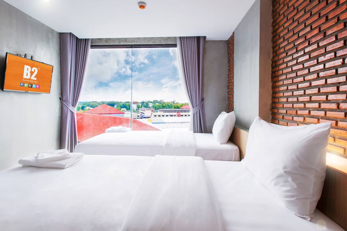 A hotel room with a large bed, a TV on the wall, and a view of buildings through the window.