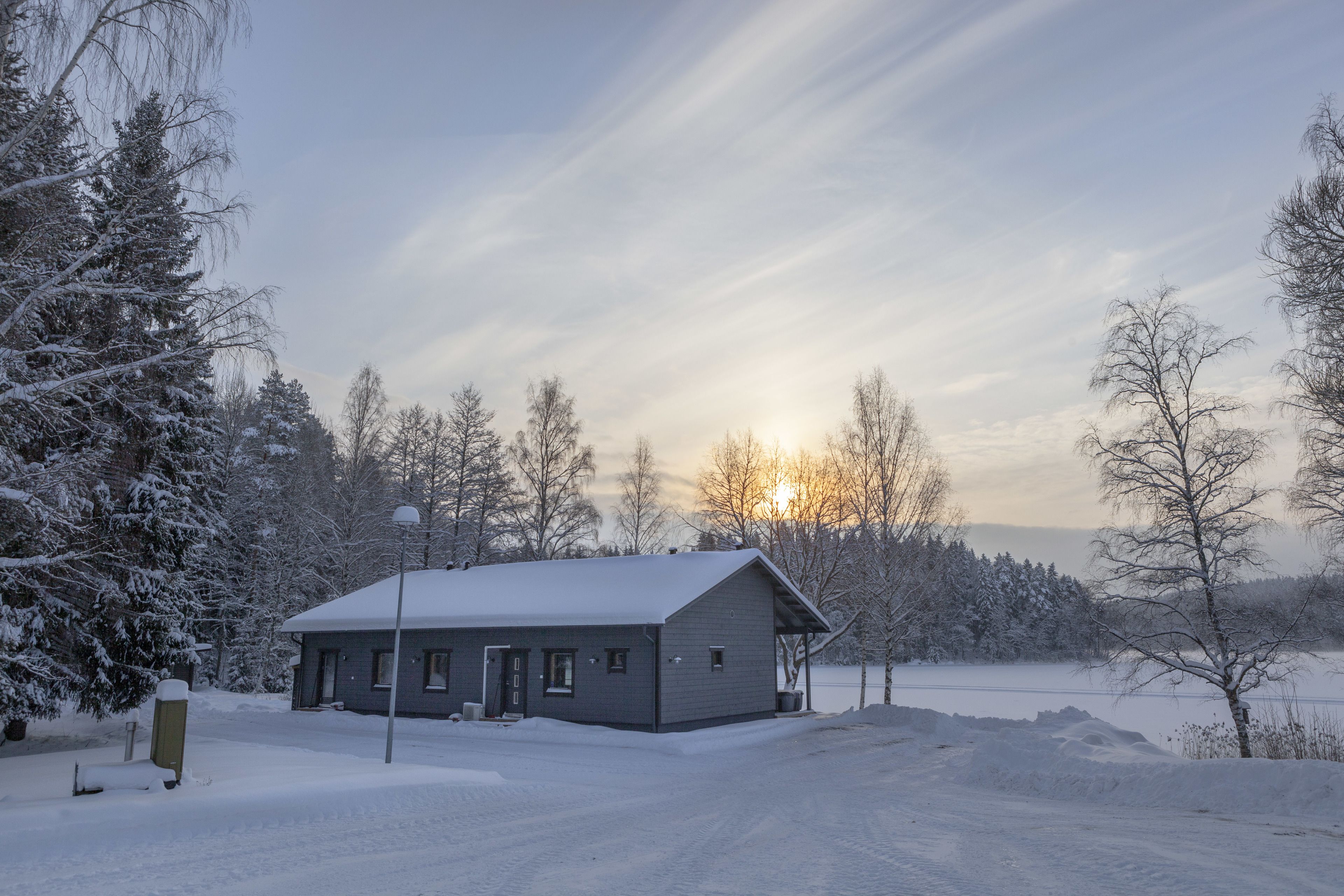 A snow-covered building with a single entrance and a small porch, surrounded by snow-laden trees and a clear sky.
