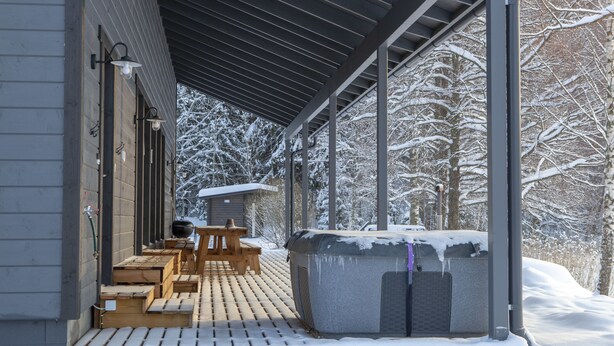 A covered outdoor seating area with wooden benches and a hot tub, surrounded by snow-covered trees. - Aulanko Lake Villa - Peace & Privacy (Hameenlinna)
