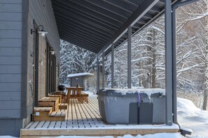 A covered outdoor seating area with wooden benches and a hot tub, surrounded by snow-covered trees. - Aulanko Lake Villa - Peace & Privacy (Hameenlinna)