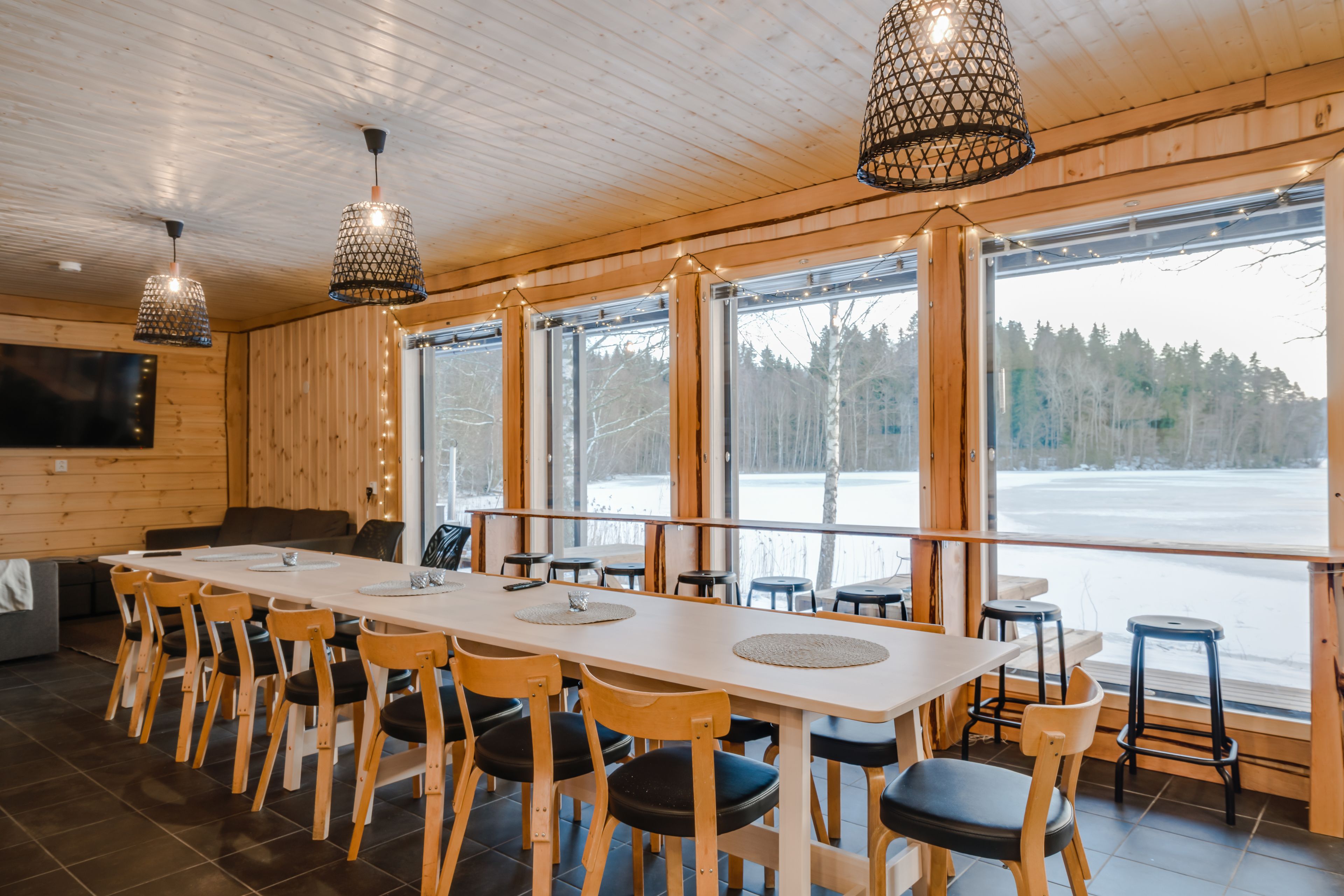 Un intérieur en bois avec une longue table à manger, des chaises et de grandes fenêtres donnant sur un paysage enneigé.