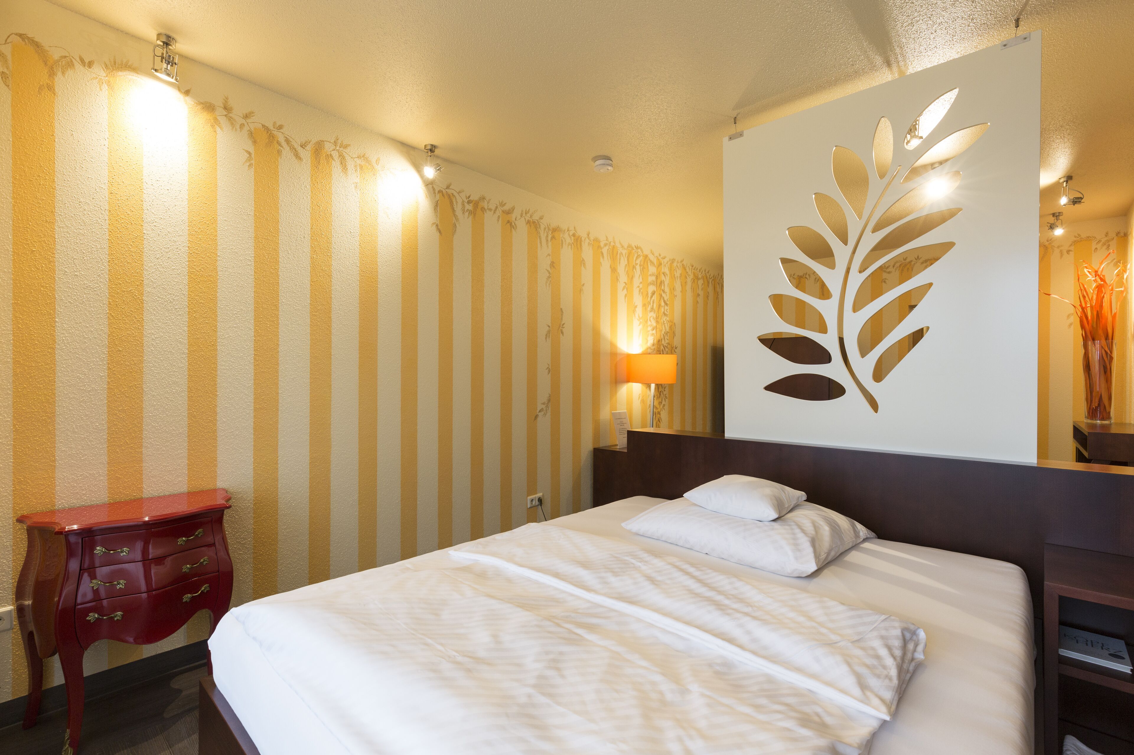 Een hotelkamer met een bed, nachtkastje, lamp en decoratief paneel.
