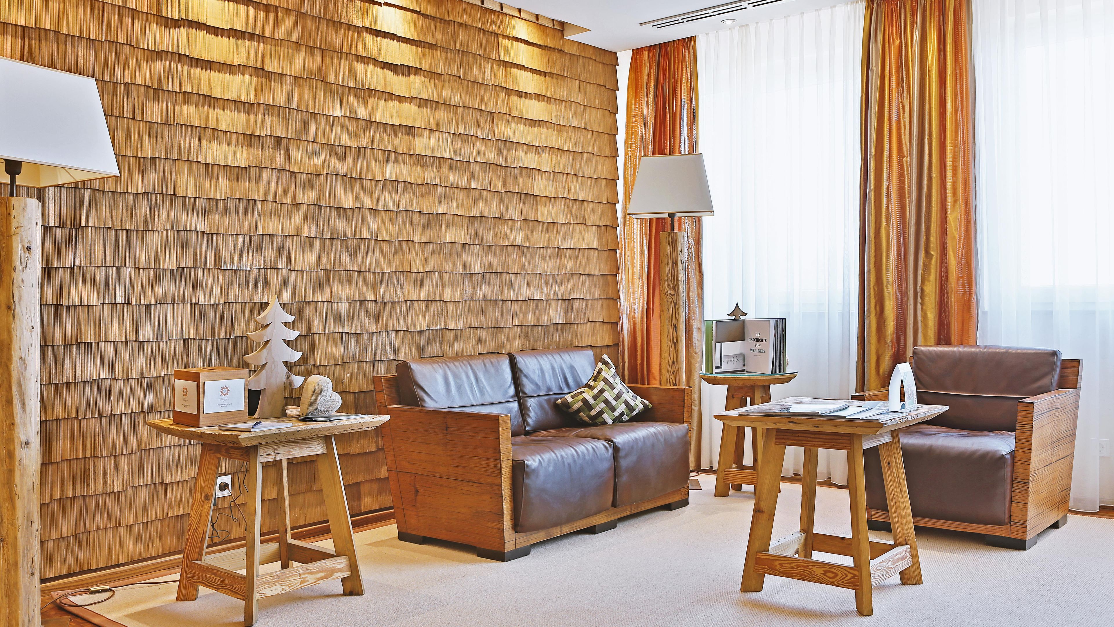 A room with a wooden wall, a leather sofa, a wooden coffee table, a wooden chair, and a lamp.
