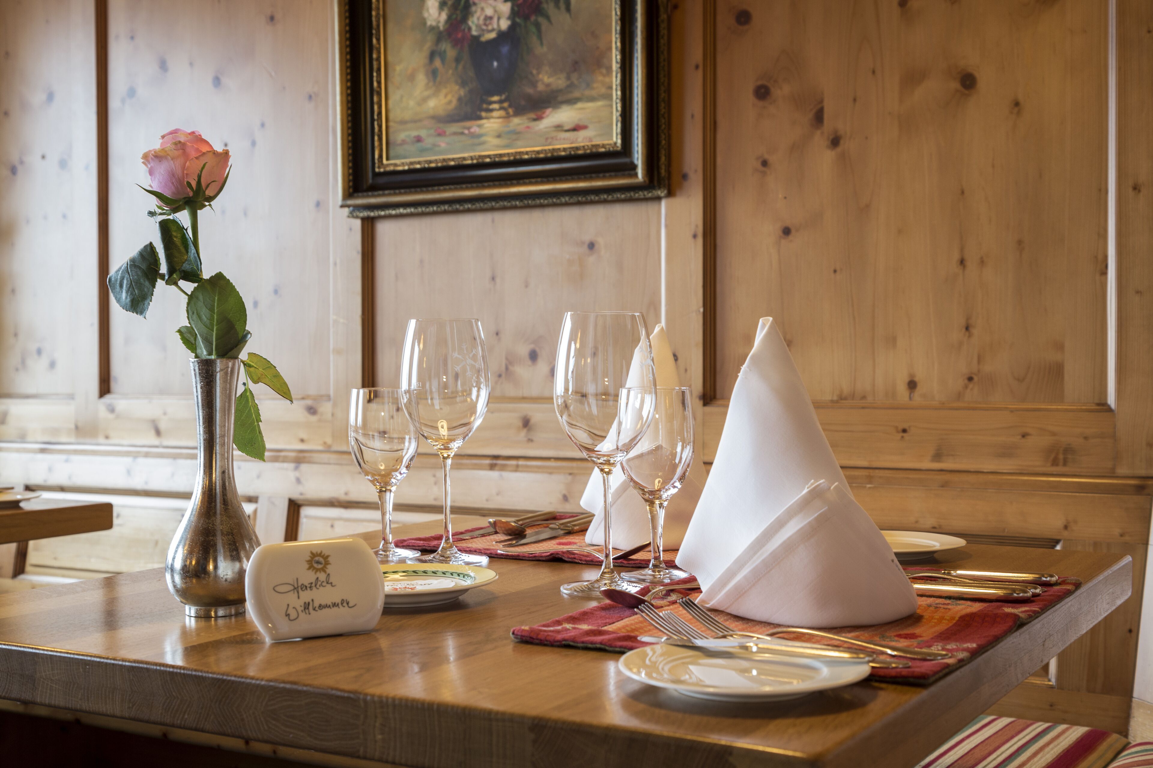 Een eettafel gedekt met wijnglazen, een wit papieren kegeltje, een roos in een vaas en een naambadje.