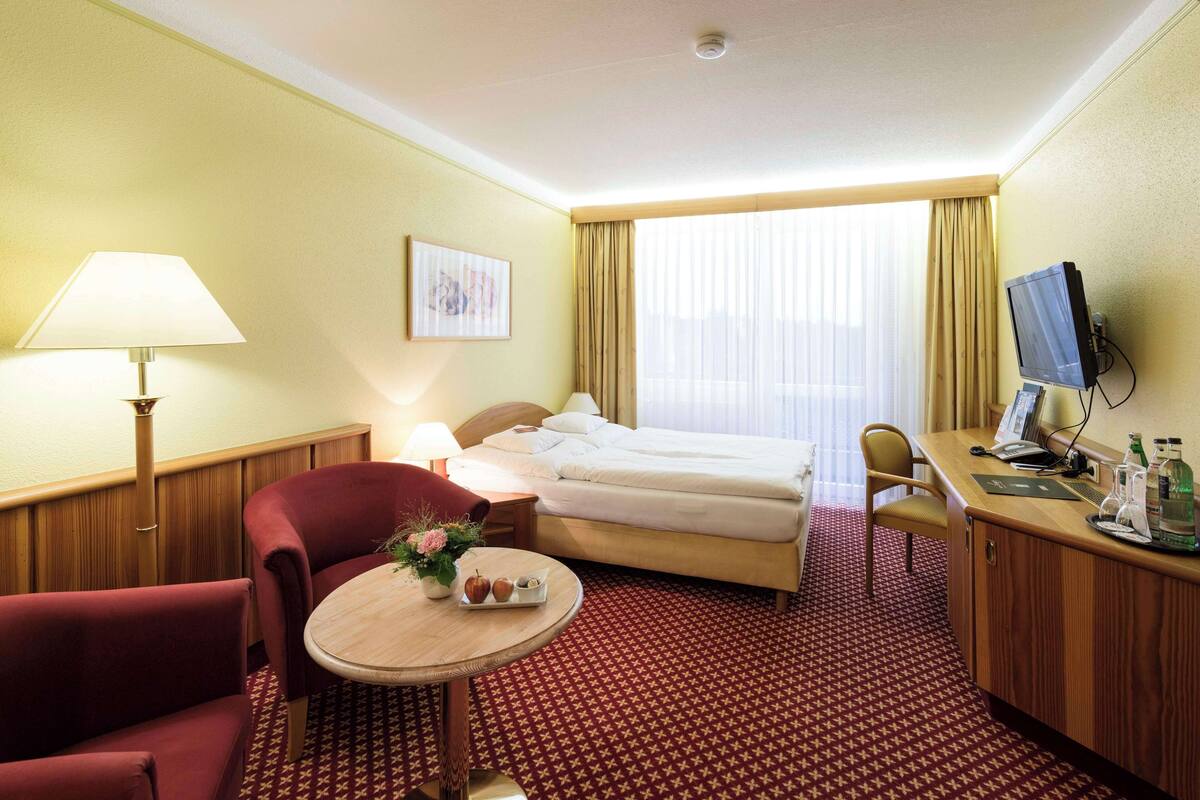 Une chambre d’hôtel équipée d’un lit, d’un bureau, d’une chaise, d’une lampe et d’une petite table sur laquelle se trouve un plateau avec divers objets.