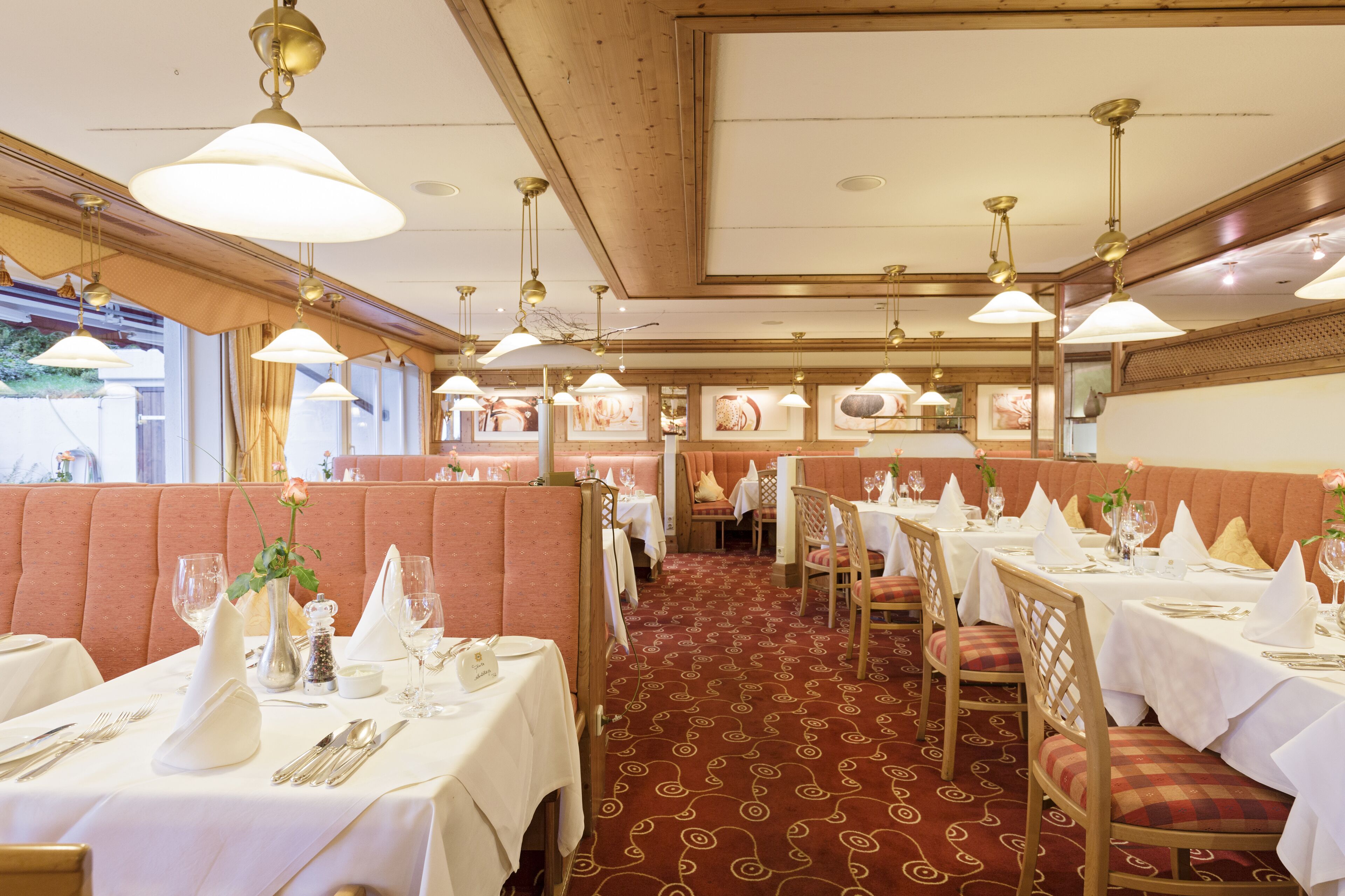 Um restaurante com cabines e mesas, cada uma com toalhas brancas, talheres e copos de vinho.