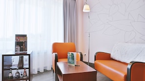 Una sala moderna con una mesa de centro de madera, un sofá naranja, una vitrina de vidrio con copas y botellas de vino, y una lámpara.