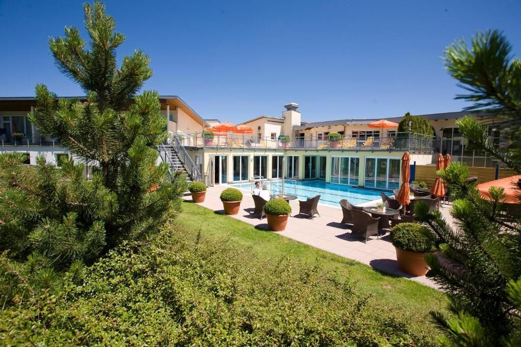 A pool area with outdoor seating, surrounded by potted plants and a building with a balcony.