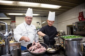 Dos chefs en una cocina con equipo de acero inoxidable y un salpicadero azulejado.