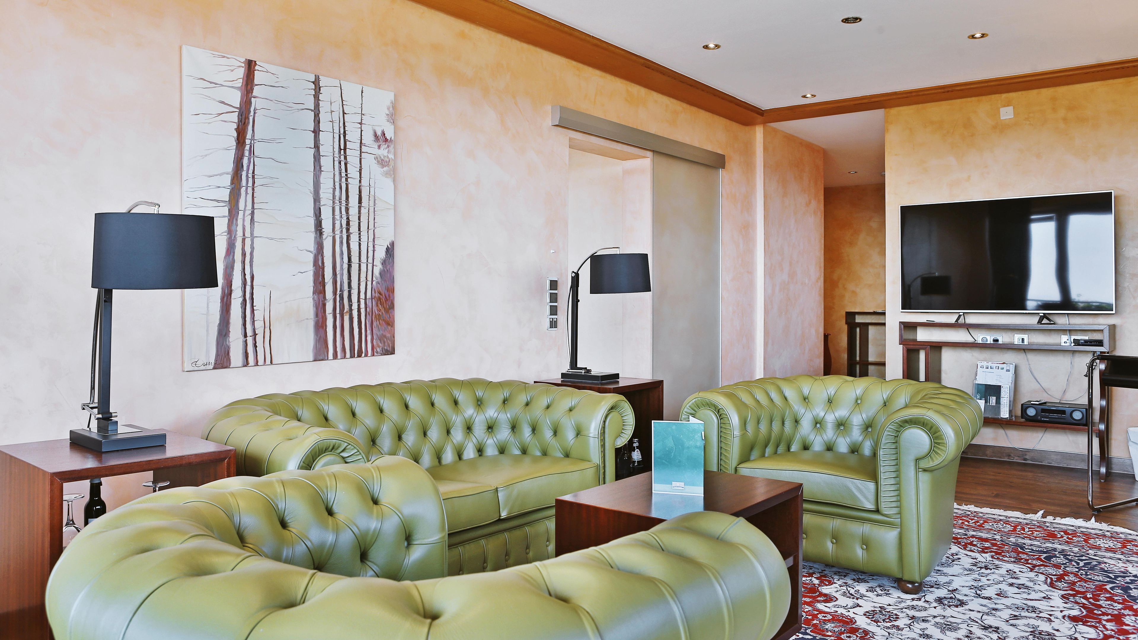 Ein Wohnzimmer mit einem grünen Ledersofa, einem Flachbildfernseher und einem Bild an der Wand.