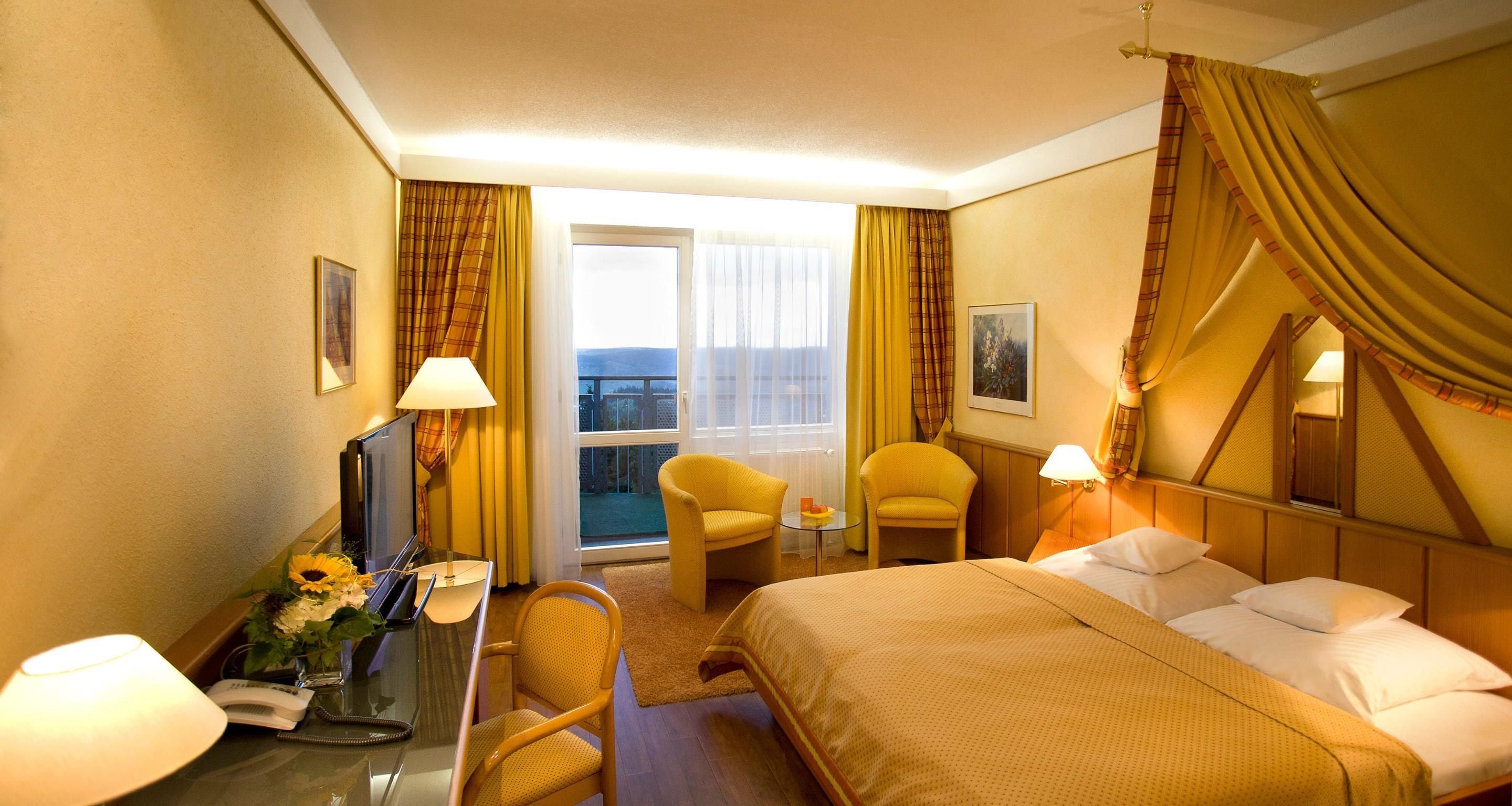 Habitación de hotel con una cama, dos sillas, un escritorio con lámpara, un teléfono y una ventana con cortinas.