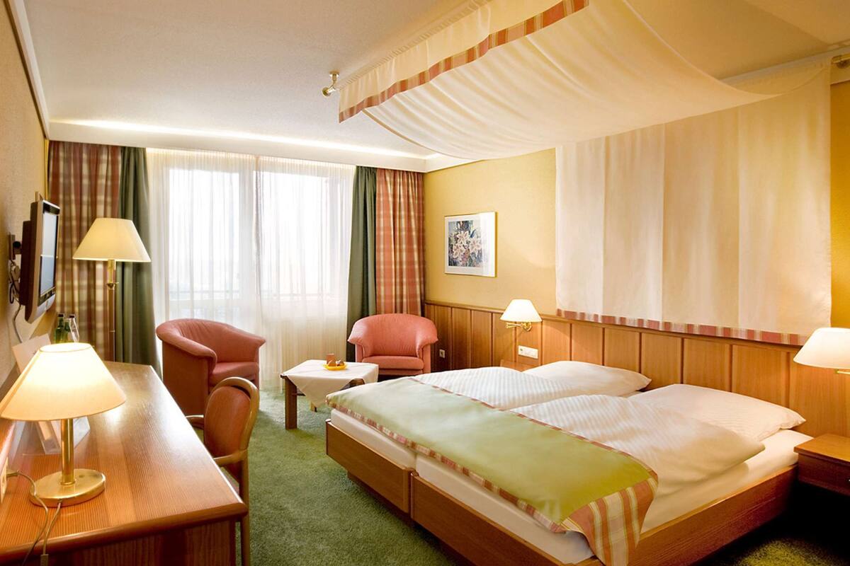 Une chambre d’hôtel comprenant un lit, deux tables de chevet, un bureau avec une lampe, une chaise, une petite table et un téléviseur.