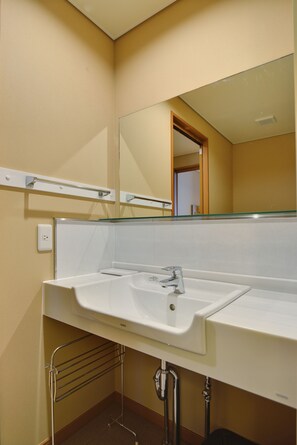 Un baño con lavamanos blanco, espejo y toallero.