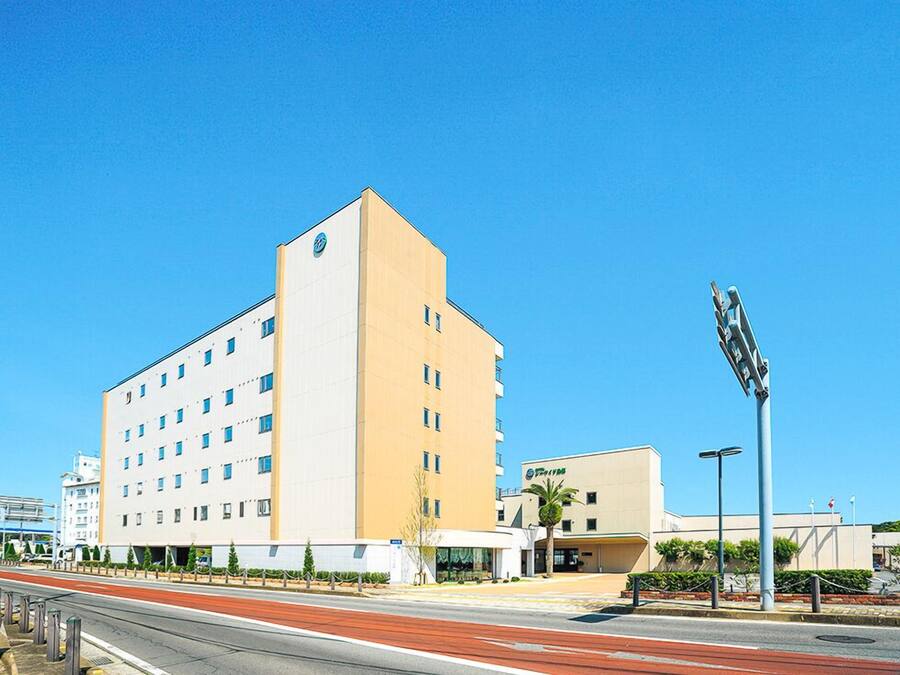 Un hôtel à plusieurs étages, doté d’une façade sobre, d’un logo bien visible en haut à gauche et d’un parking situé à l’avant.