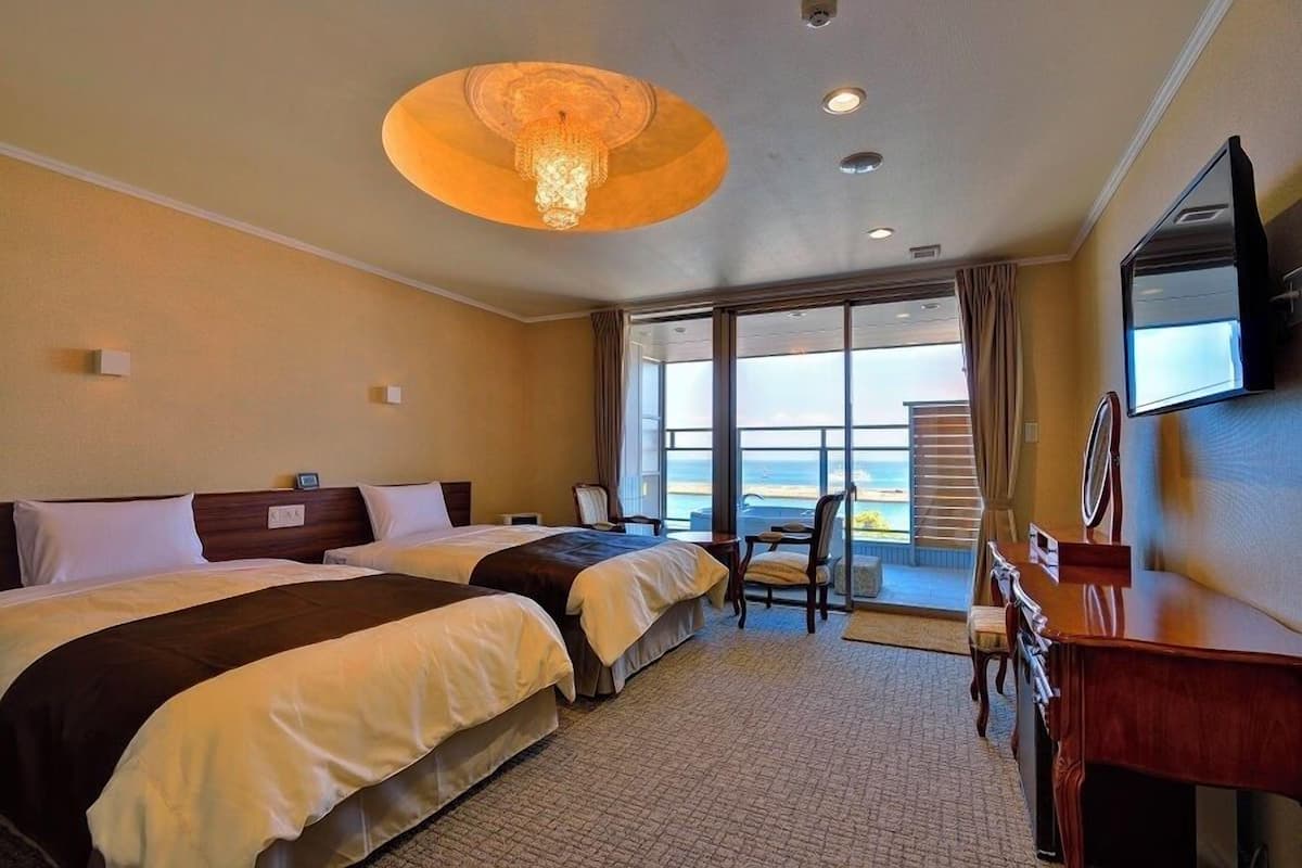 A hotel room with two beds, a desk, a chair, a television, and a large window with a view.