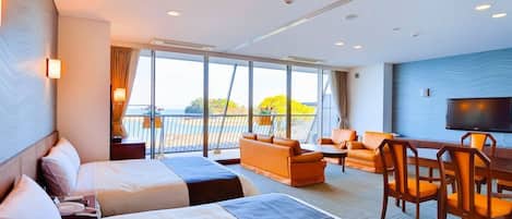 A hotel room with two beds, a sofa, a dining table with chairs, a TV, and a balcony with a view.