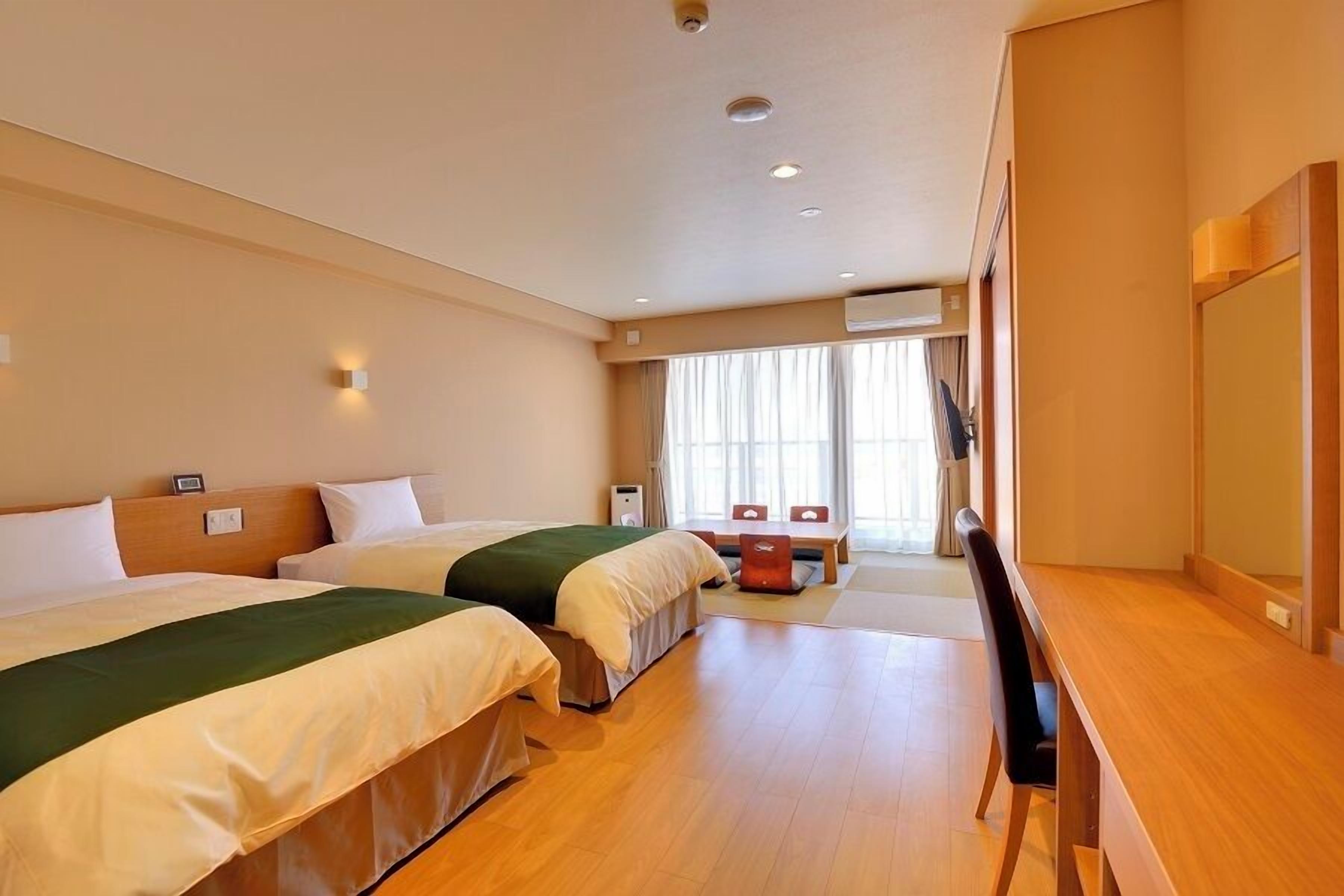 A hotel room with two beds, a desk, and a TV.