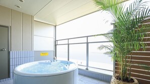 Une salle de spa équipée d’un bain à remous, d’une plante en pot et d’une grande fenêtre laissant entrer la lumière naturelle.