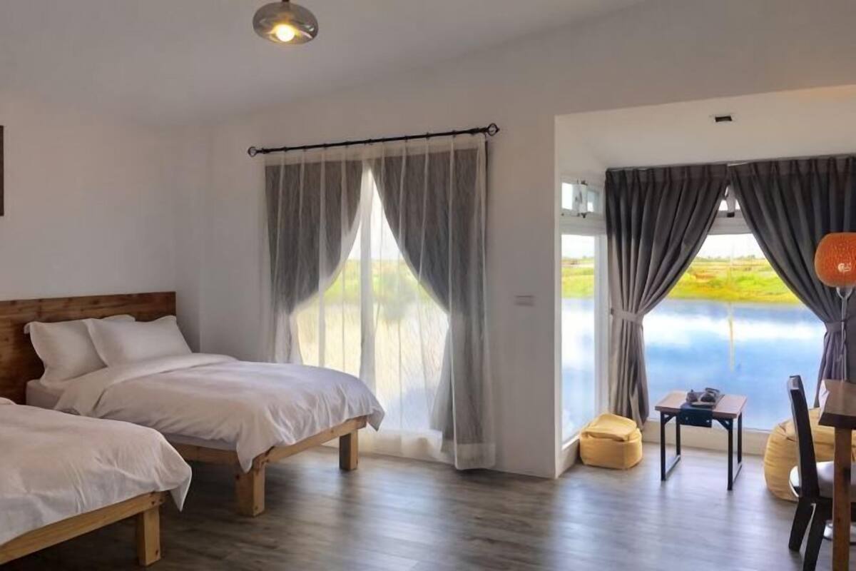 A bedroom with two beds, a wooden headboard, a small table, and a view of the outdoors.
