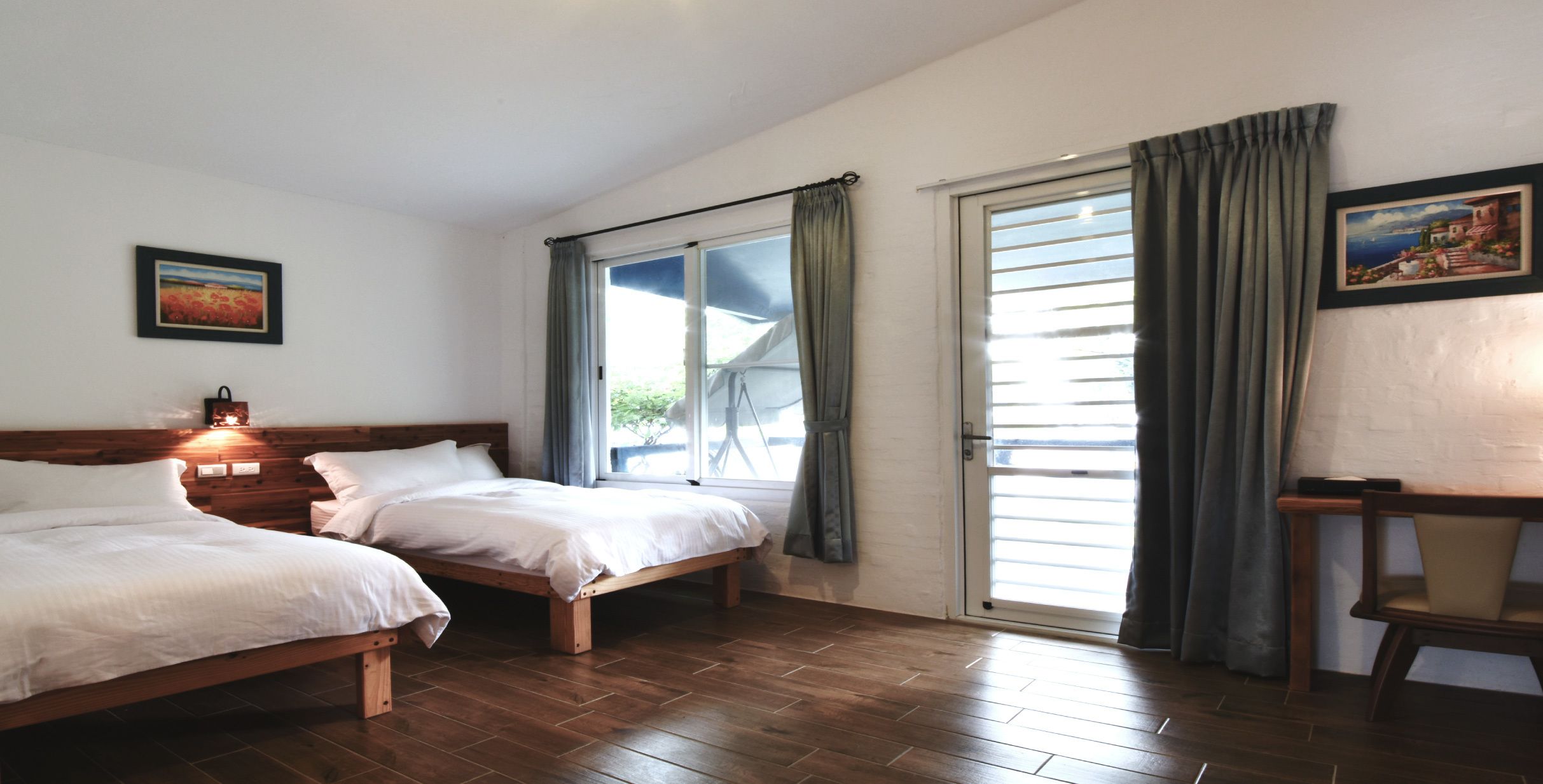 A room with two beds, a wooden floor, a sliding glass door, and a painting on the wall.