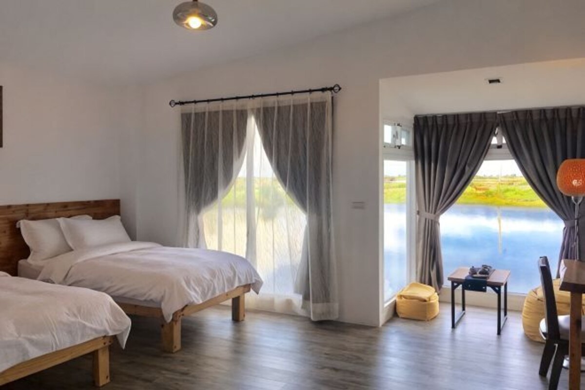 Un dormitorio con dos camas, cabecero de madera, una mesita y vistas al exterior.