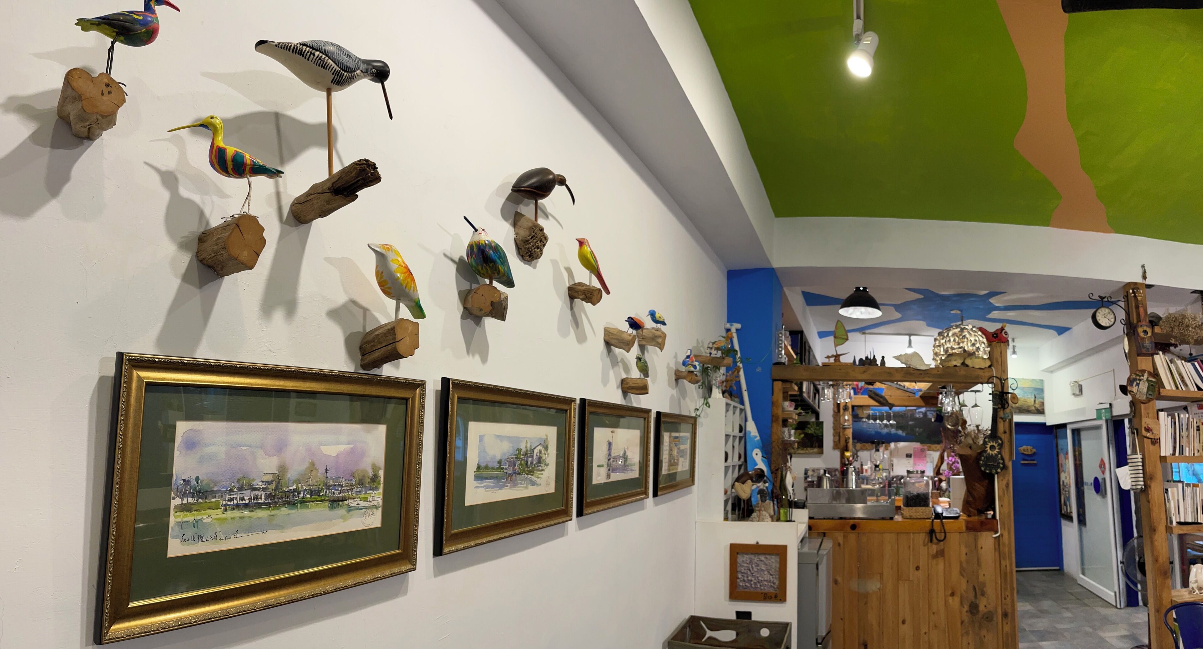 A hallway with framed watercolor paintings, wooden bird sculptures, and a wooden counter with various items.