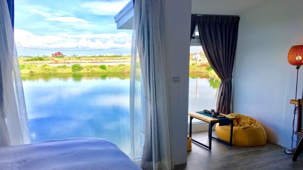 A room with a view of a calm body of water, a bed, a table with tea set, and a yellow bean bag. - LanJen Villa B&B (Tainan)