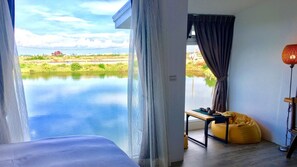 A room with a view of a calm body of water, a bed, a table with tea set, and a yellow bean bag. - LanJen Villa B&B (Tainan)